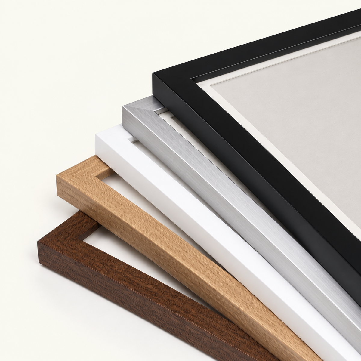 Four picture frame profiles stacked diagonally on a light cream background, showing black, silver, white, and natural wood finishes.